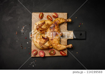 Whole fried chicken with spices on a wooden board on a black table 114199569