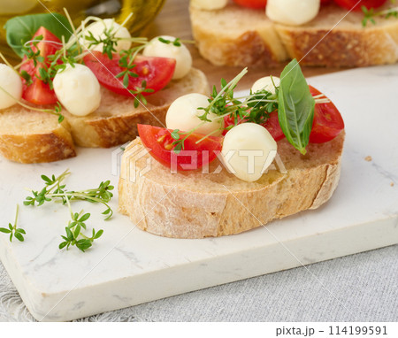 Round mozzarella, cherry tomatoes and microgreens on a piece of white bread Round mozzarella, cherry tomatoes and microgreens on a piece of white bread 114199591