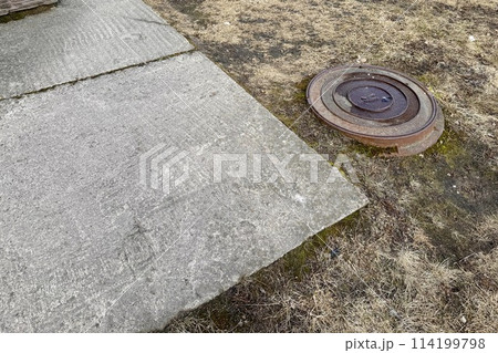 A rusty iron hatch with a pattern is located next to a dry grass pedestrian road during the daytime. Close-up 114199798