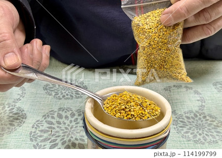 The seller's hand fills bee perga as called ambrosia in a plastic container. Top view. Close-up with a spoon in a container. Healthy eating. The energy of life The seller's hand fills bee perga as called ambrosia in a plastic container. Top view. Close-up with a spoon in a container. Healthy eating. The energy of life 114199799