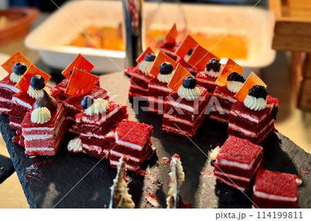 The portions of red layered cream cake with blueberry on a black stand on the counter of the restaurant. Close-up The portions of red layered cream cake with blueberry on a black stand on the counter of the restaurant. Close-up 114199811