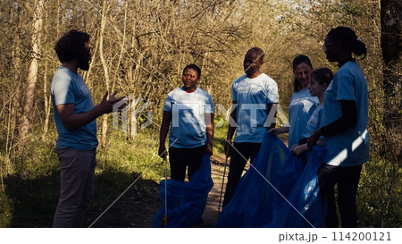 Team of activists picking up plastic waste to recycle and collect rubbish, cleaning the forest natural environment for conservation. People doing voluntary work to save the planet. Camera B. 114200121
