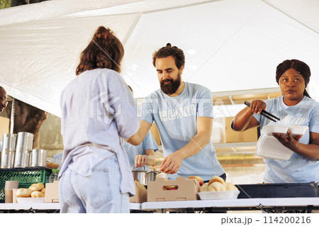 Charitable volunteers distributing free meals to homeless and needy individuals at an outdoor local food bank. Hunger relief team supporting and providing food assistance to the less fortunate. Charitable volunteers distributing free meals to homeless and needy individuals at an outdoor local food bank. Hunger relief team supporting and providing food assistance to the less fortunate. 114200216