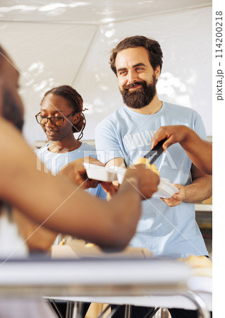 Portrait of a friendly volunteer distributing free food to a crippled homeless person. Detailed image shows a caucasian man helping during a food drive to serve hot meals to the poor and needy. Portrait of a friendly volunteer distributing free food to a crippled homeless person. Detailed image shows a caucasian man helping during a food drive to serve hot meals to the poor and needy. 114200218