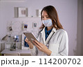 A female doctor in a mask and white uniform uses a tablet in her work. Technologies 114200702