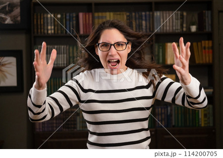 Portrait of an angry woman boss with glasses in the office looks at the camera and screams Portrait of an angry woman boss with glasses in the office looks at the camera and screams 114200705