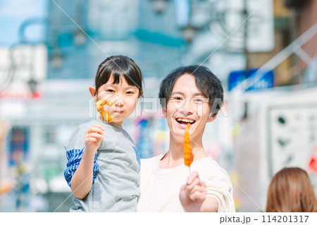 大阪観光で通天閣を背に名物の串かつを食べる親子 114201317