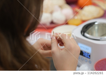 The process of making a massage candle using ingredients oils and wax measure weigh stir add close-up of women's hands. food thermometer measure wax temperature women's party women witches witchcraft 114202281