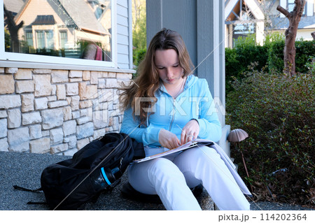 teenager girl does homework on porch of house she writes with pencil in large notebook notebook in folder next to backpack autumn summer sit on threshold beautiful young woman writes draws solves teenager girl does homework on porch of house she writes with pencil in large notebook notebook in folder next to backpack autumn summer sit on threshold beautiful young woman writes draws solves 114202364