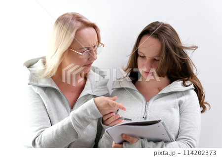 mother and daughter solve math problems together doing homework Girl writes in notebook with pen woman shows finger hint mutual understanding help good relationships adolescence in white studio 114202373
