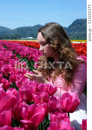 a young girl teenager stands in beautiful bright pink Corolla tulips inhale the fragrance of flowers straighten her hair look into the distance beautiful field in spring unusually bright color 114202375