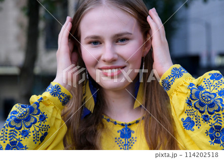beautiful Ukrainian woman in a yellow-blue embroidered shirt looks into the frame smiles straightens close-up face earrings in the form of the flag of Ukraine Victory fun joy strength Freedom Will 114202518