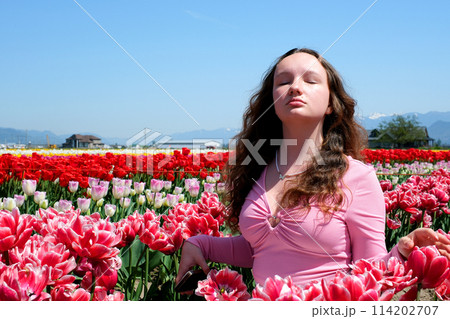 a beautiful young girl raised her face in the wind looks closed her eyes inhales fresh air stands in a field of tulips red tulips with a white border against clear blue sky freshness joy freedom will 114202707