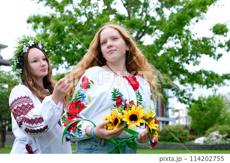 girl are sitting in park waiting for holiday to weave hair braid pigtail wreaths of flowers on head help friend tenderness beauty young hairdresser young women are preparing for celebration 114202755