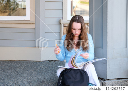 High school student girl is flipping through pages. Attractive young woman is holding copybook. Beautiful girl isolated on white background. 114202767