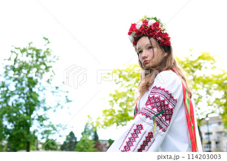 beautiful Ukrainian young woman tender girl in a large red wreath of bright pink white red flowers braiding ribbons in hair wind tenderness cleanliness peace in Ukraine Peacetime people Real life 114203003