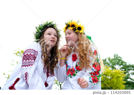 Midsummer. Two girls in the Slavic clothes weave braids in the hair near the fire. Midsummer. Two girls in the Slavic clothes weave braids in the hair near the fire. 114203005