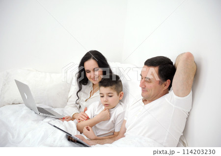 Three man, woman and little boy take selfie in smartphone in bed Three man, woman and little boy take selfie in smartphone in bed 114203230