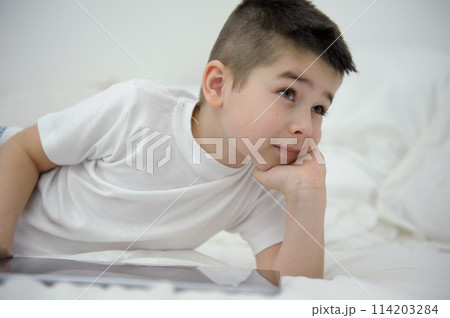 boy of seven or eight years old sits on bed leaned on arm lay down on white blanket looks into distance sly thoughtful look plans day Thinks about the prospects for future dreams desires black hair boy of seven or eight years old sits on bed leaned on arm lay down on white blanket looks into distance sly thoughtful look plans day Thinks about the prospects for future dreams desires black hair 114203284