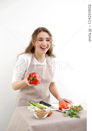 bright sincere laugh of a young woman in her hands with red pepper cooking a delicious lunch communication online training cooking course chef young girl on a white background 114203608