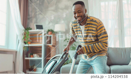 Cheerful african american man vacuuming an apartment. Minimalist interior cozy living room on background Cheerful african american man vacuuming an apartment. Minimalist interior cozy living room on background 114204538