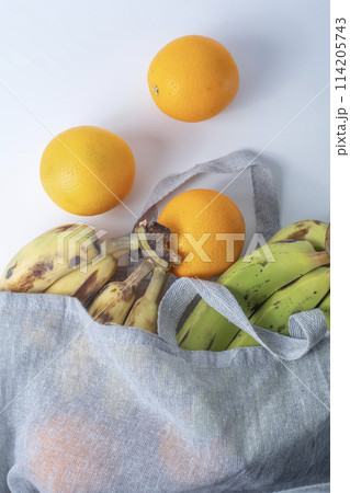 Fresh bananas and oranges in a reusable bag on a white background. Fresh bananas and oranges in a reusable bag on a white background. 114205743