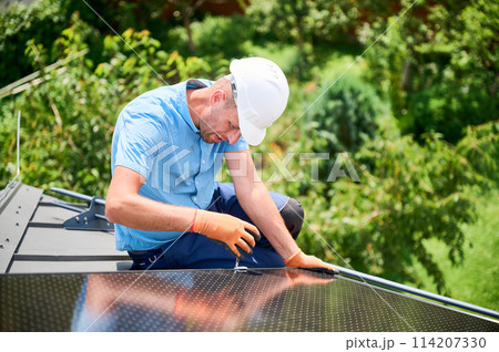 Worker building photovoltaic solar panel system on rooftop of house. Man engineer in helmets and gloves installing solar module with help of hex key outdoors. Alternative energy generation concept. 114207330