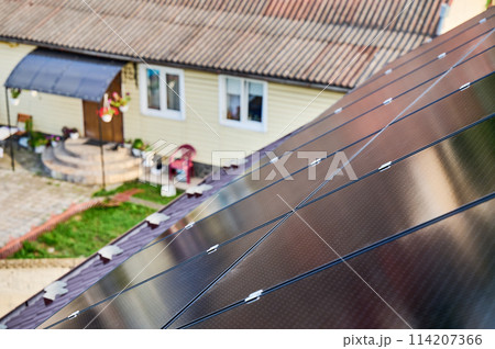 Solar panels installed on sloped roof of suburban home. Panels angled to capture sunlight. Installation of solar batteries on rooftop of house. Concept of alternative energy sources in modern life. 114207366