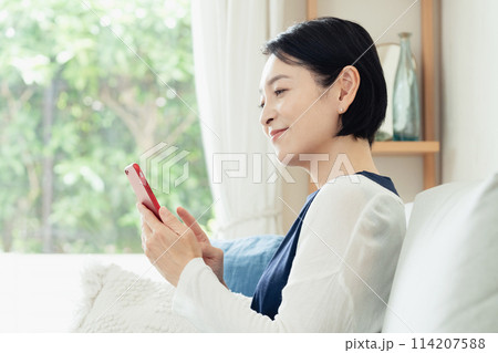 リビングでスマートフォンを操作する主婦 リビングでスマートフォンを操作する主婦 114207588