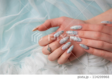 Female hands with blue nail design on blue silk background. Female hands with blue nail design on blue silk background. 114209968