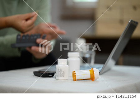 Focus on prescription pill bottles on table in living room and senior couple sitting on background Focus on prescription pill bottles on table in living room and senior couple sitting on background 114211154