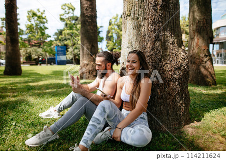 Man and woman relaxing with digital tablet in park after sports training 114211624