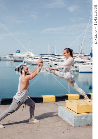 Male coach helping young woman exercising on pier. 114211658