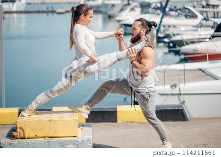 Male coach helping young woman exercising on pier. Male coach helping young woman exercising on pier. 114211661