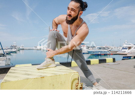 Sports lifestyle. Happy young caucasian bodybuilder stretching on the sea shore. Sports lifestyle. Happy young caucasian bodybuilder stretching on the sea shore. 114211666