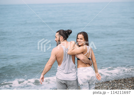 Young fitness couple embracing standing on beach, looking at horizon Young fitness couple embracing standing on beach, looking at horizon 114211697