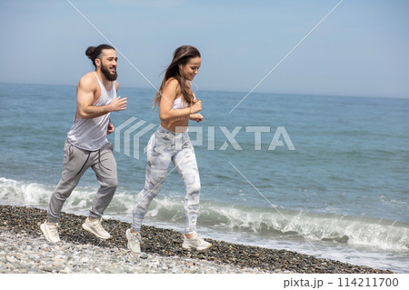 Happy couple running together beside the water at the beach 114211700