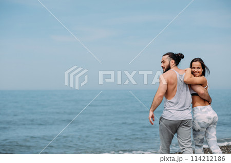 Young fitness couple embracing standing on beach, looking at horizon Young fitness couple embracing standing on beach, looking at horizon 114212186