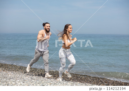 Happy couple running together beside the water at the beach 114212194