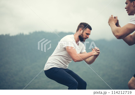 Two male athletic friends doing box jump outdoor on top of the mountain. 114212719