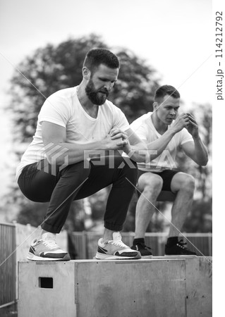 Caucasian male athletic friends doing box jump outdoor on top of the mountain. Caucasian male athletic friends doing box jump outdoor on top of the mountain. 114212792