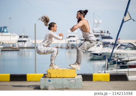 Female and male athlete is performing box jumps outdoor. Female and male athlete is performing box jumps outdoor. 114213398