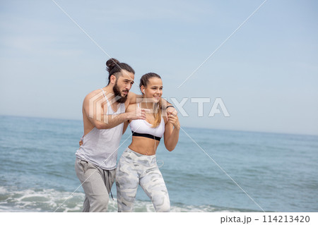 Happy caucasian sportive couple walking together on a beach 114213420