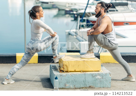Young beautiful couple doing stretching exercises at the ocean pier Young beautiful couple doing stretching exercises at the ocean pier 114213522