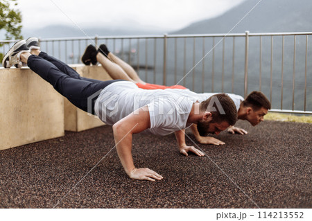 Two young athletes doing push-ups outdoors. 114213552