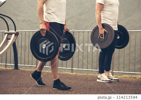 Caucasian muscular men with weight plates preparing to outdoor workout. Caucasian muscular men with weight plates preparing to outdoor workout. 114213594