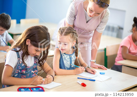 Teacher helping kids with their homework in classroom at school 114213950