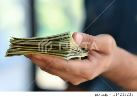 A persons hand holds a towering stack of money, showcasing abundance, success, and financial prosperity. A persons hand holds a towering stack of money, showcasing abundance, success, and financial prosperity. 114218235