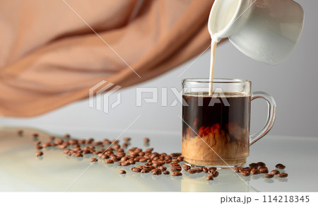 Pouring milk in black coffee. 114218345