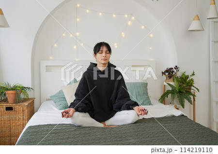 Yoga mindfulness meditation. Young healthy woman practicing yoga in bedroom at home. Woman sitting in lotus pose on bed meditating smiling relaxing indoor. Girl doing breathing practice. Yoga at home 114219110